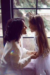 Mother and daughter in dresses stand at a large window in the studio at christmas