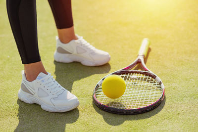 Low section of woman standing by ball and tennis racket on court