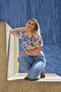 Portrait of a smiling young woman sitting against wall