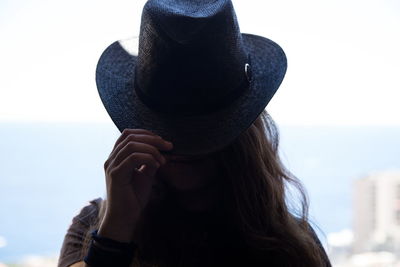 Woman covering face with hat while standing outdoors