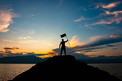 Silhouette man standing on rock by sea against sky during sunset