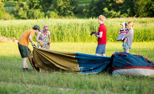 Pilot with people standing by hot air balloon on grassy field during sunset