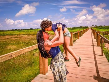 Rear view of couple walking on wood against sky