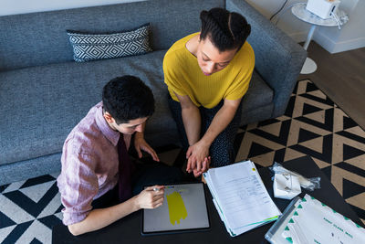 High angle view of male and female colleagues discussing over graphics tablet at table in office