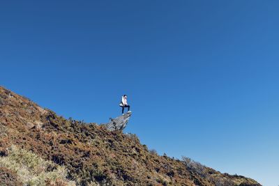 Low angle view of man on rock against clear blue sky