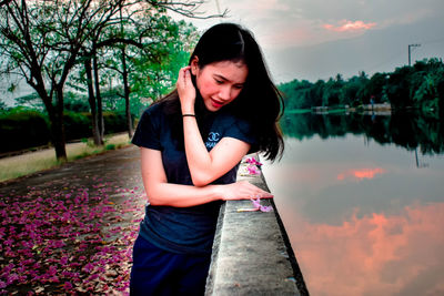 Beautiful woman standing on mobile phone against lake