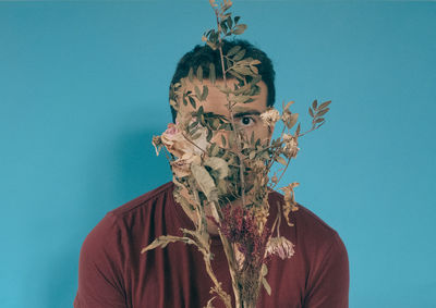 Close-up portrait of man with dry plants against blue background