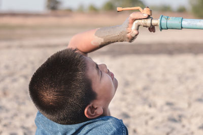 Close-up of boy looking at faucet during drought on field