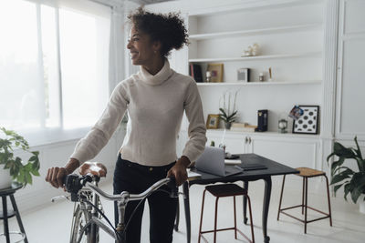 Mid adult woman leaving her home office, pushing bicycle