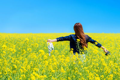 Rear view of woman with camera standing at rape field