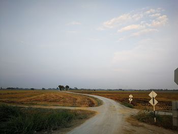 Empty road amidst agricultural field against sky