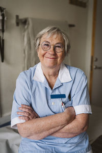 Portrait of smiling senior female doctor standing with arms crossed