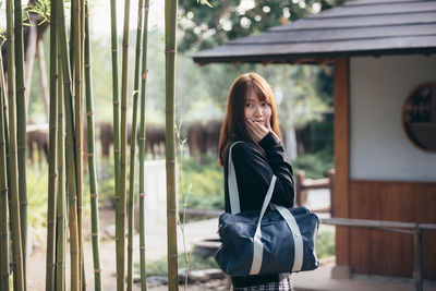 Portrait of smiling young woman standing against trees