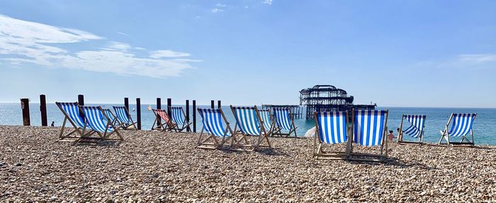 Wooden chairs on beach against blue sky