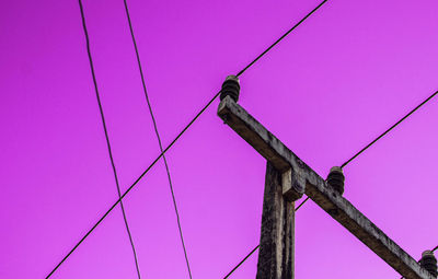 Low angle view of bird perching on cable against pink sky