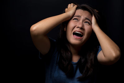 Scared young woman screaming while standing against black background