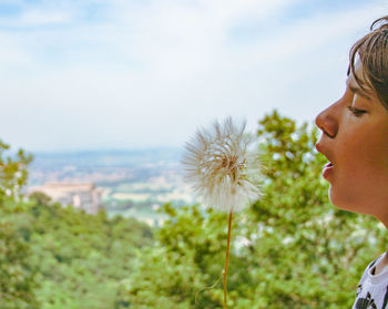Close-up portrait of young woman with dandelion against sky