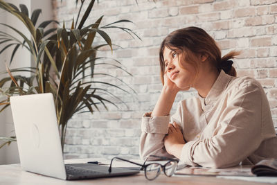 Young woman using mobile phone while sitting against wall