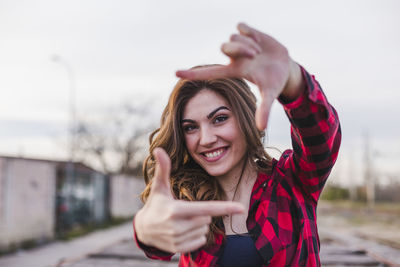 Portrait of smiling woman making finger frame against sky