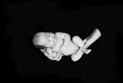Cropped hands of parent holding naked baby boys against black background
