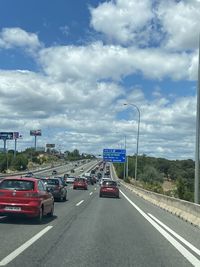 Vehicles on road against cloudy sky