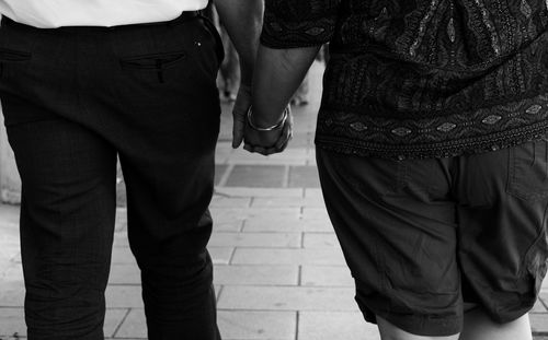 Midsection of couple holding hands while walking on footpath in city