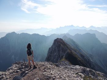 Rear view of young woman with backpack standing on mountain against sky