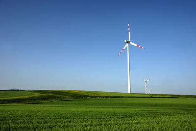 Wind turbines on grassy field against clear sky