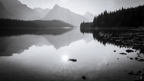 Sun reflecting in still alpine lake surrounded by mountains, monochromatic, jasper np, canada