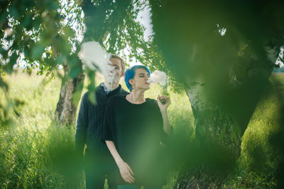 Friends smoking while standing by tree on field