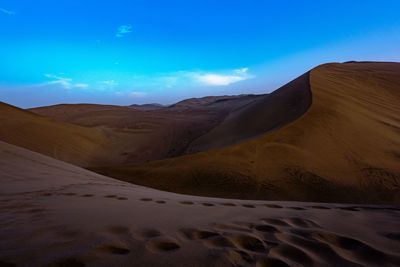 Scenic view of sand dunes in desert against cloudy sky