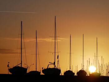 Silhouette sailboats moored in harbor against sky during sunset