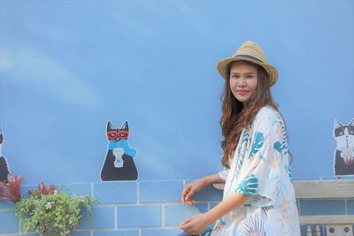 Woman wearing hat standing against blue wall with cat painting 