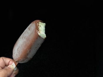 Close-up of hand holding ice cream over black background