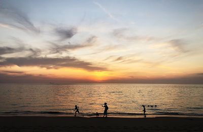 Silhouette people on beach against sky during sunset