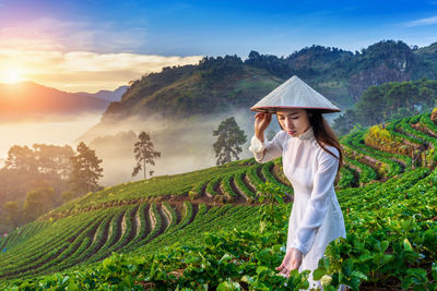 Woman wearing asian style conical hat while standing on agricultural field