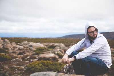 Young man on rock against sky