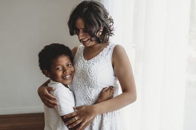 Mid-level view of smiling son being hugged by smiling mother in studio