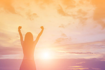 Silhouette woman with arms raised against sky during sunset