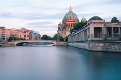 View of buildings by river against sky in city