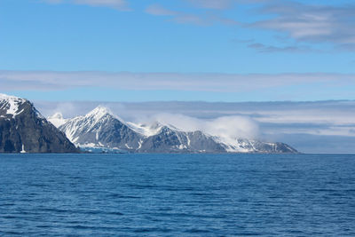 Scenic view of sea and snowcapped mountains against sky