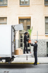 Male and female movers unloading potted plant from truck on street in city