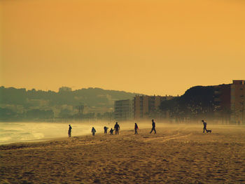 Silhouette people on beach against sky during sunset