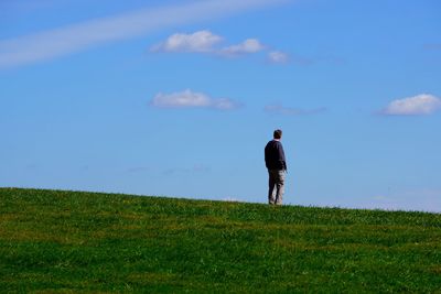 Rear view of man walking on field against sky
