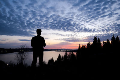 Silhouette man standing by lake against sky during sunset