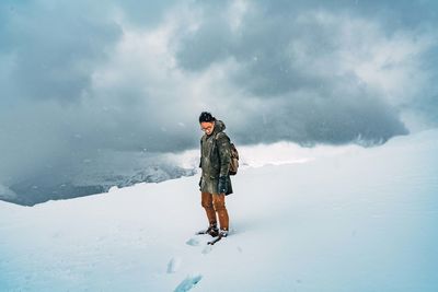 Man standing on snowy land against cloudy sky