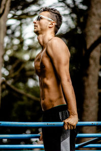 Young man looking away while standing on tree