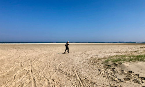 Rear view of woman walking at beach against clear blue sky