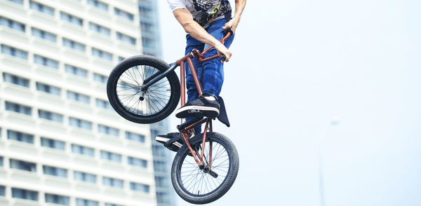 Low section of man practicing stunt on bicycle against clear sky