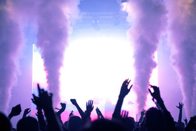 Concert crowd partying at live concert. bright stage lights, raised arms and smoke cannons, backlit